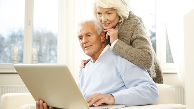 Paar sitzt auf einer Couch und schaut gemeinsam auf einen Laptop in einem hellen Raum.